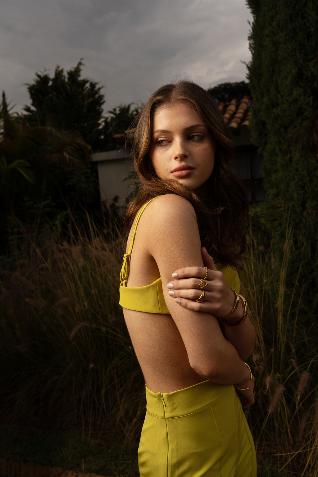 Full‑length of a model wearing Conventus IV Pants and mini top featuring green tone, high-waisted and wide‑leg cut. Standing in the garden of a luxury italian villa.
