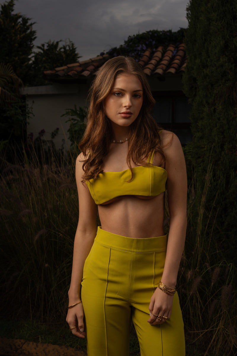 Full‑length of a model wearing Conventus IV Pants and mini top featuring swirling green pattern, high-waisted and wide‑leg cut. Standing in the garden of a luxury italian villa.